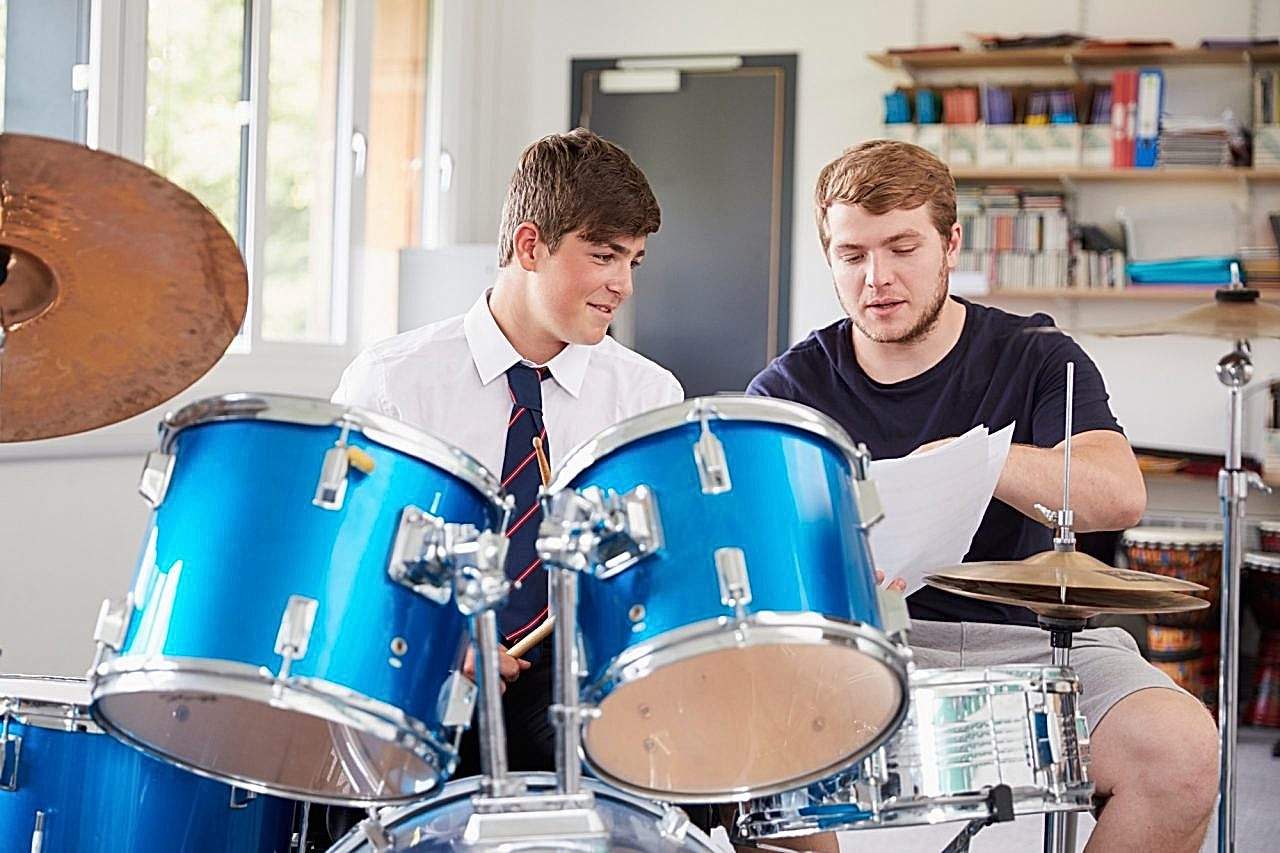Male Pupil With Teacher Playing Drums In Music Lesson